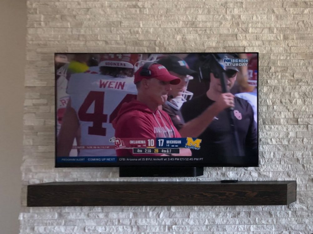 TV mounted on a white stacked-stone wall above a dark wood mantel