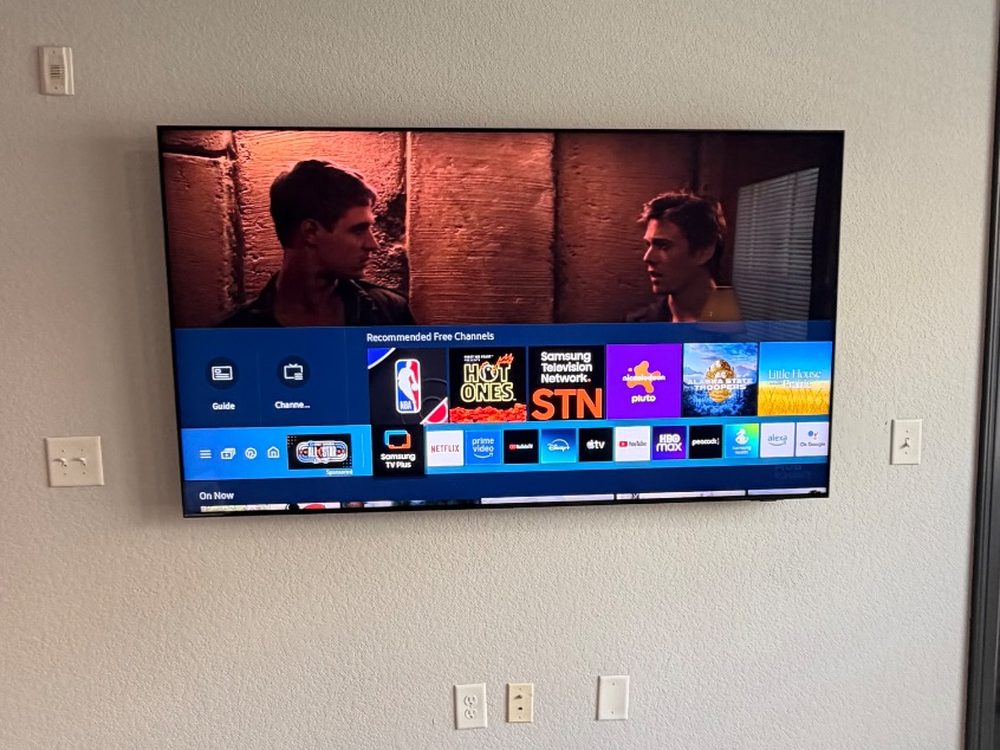 Samsung TV mounted flat on a textured wall, outlets below